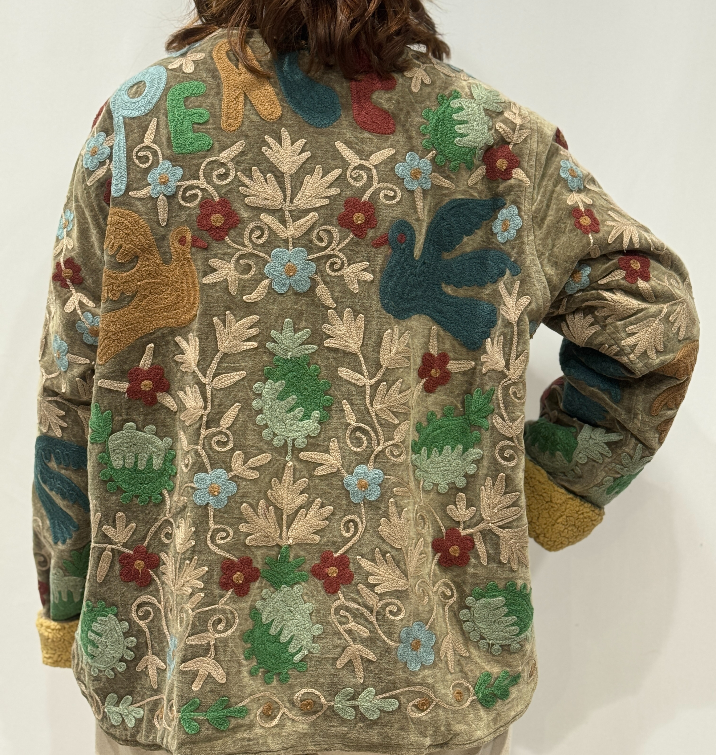 Détail du dos de la veste Amira avec motifs floraux, oiseaux brodés et inscription "peace" en haut.