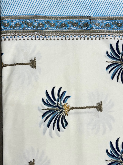 Nappe Samira, une nappe ronde de 150 cm sur fond blanc et des palmiers imprimés bleus.