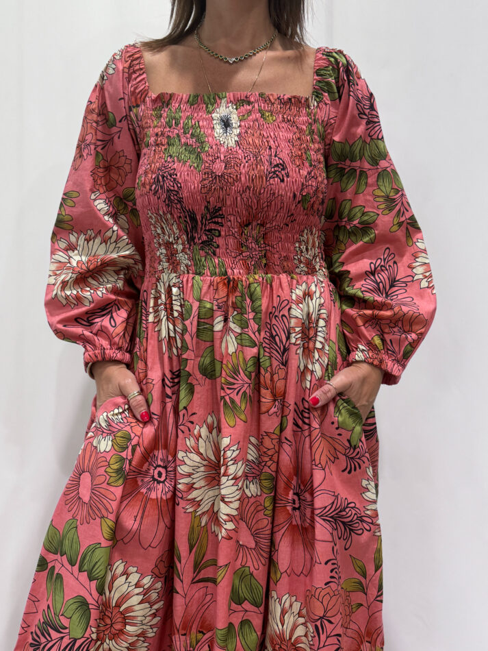 Robe Amira Rose, une robe longue smockée. Fluide et 100 % coton. Elle est rose avec des imprimée fleurit.