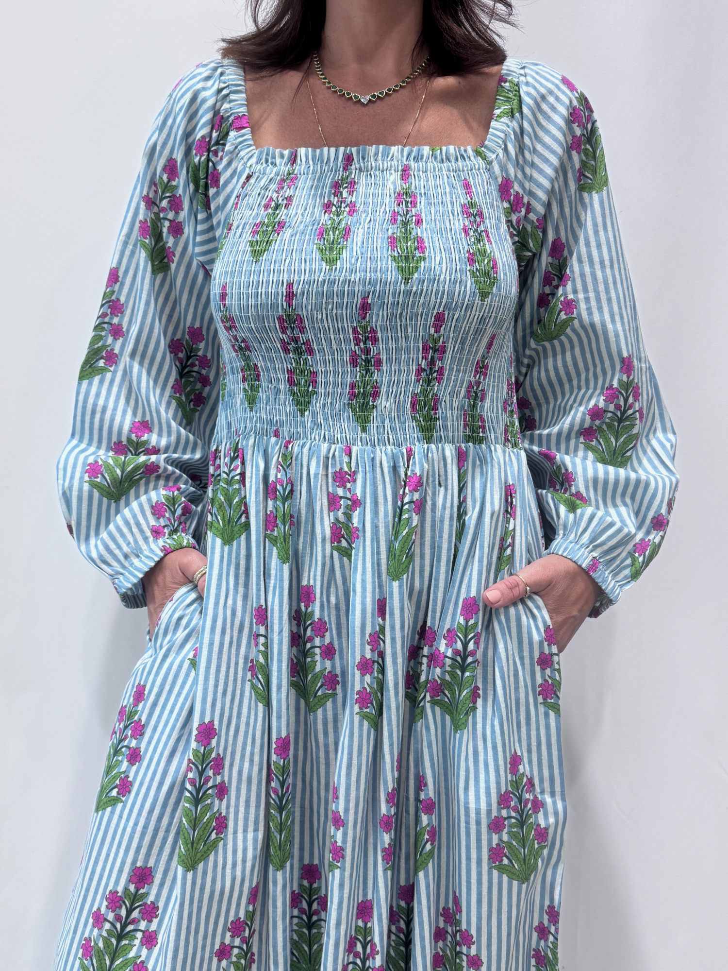 Robe Naya Bleu, une robe longue smockée. Fluide et 100 % coton. Elle est rayée avec des imprimés de fleurs.