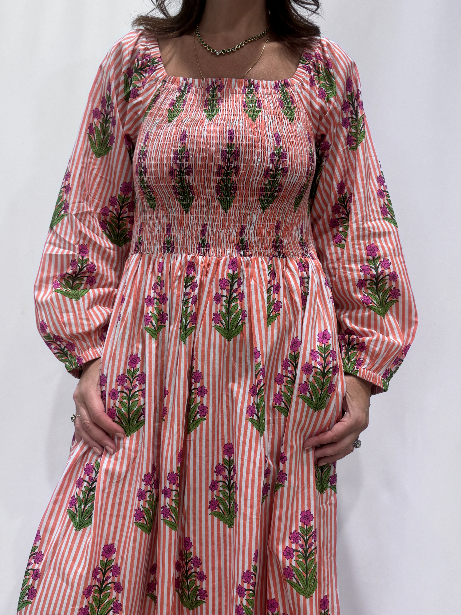 Robe Naya Saumon fleurs mauves, une robe longue smockée. Fluide et 100 % coton. Elle est rayée avec des imprimés de fleurs.
