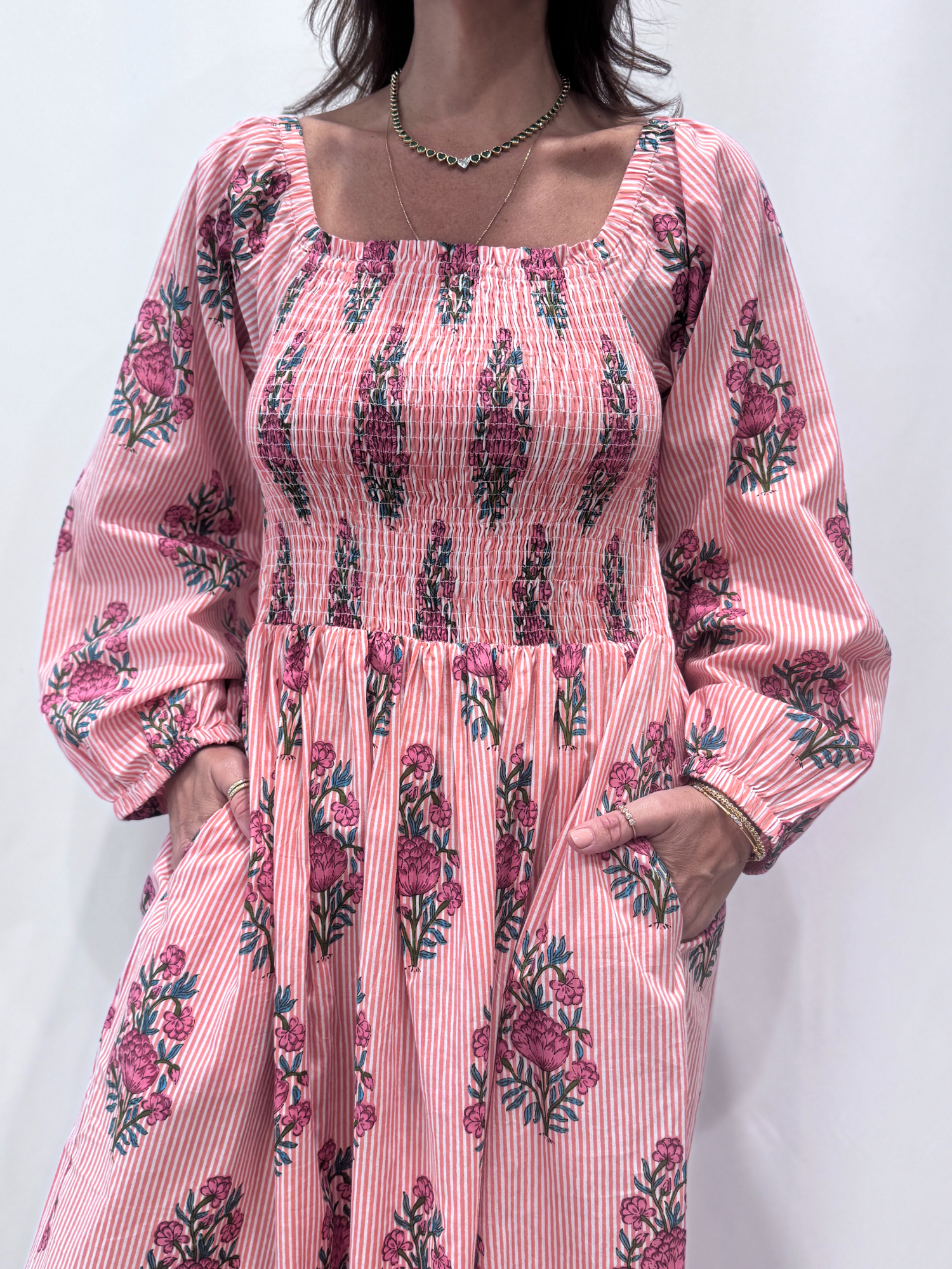 Robe Naya Saumon fleurs roses, une robe longue smockée. Fluide et 100 % coton. Elle est rayée avec des imprimés de fleurs.