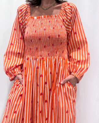 La robe Pyaar Orange, une robe longue manches longues, smockée à rayures et imprimés de coeurs. Une robe tendance pour cet été.