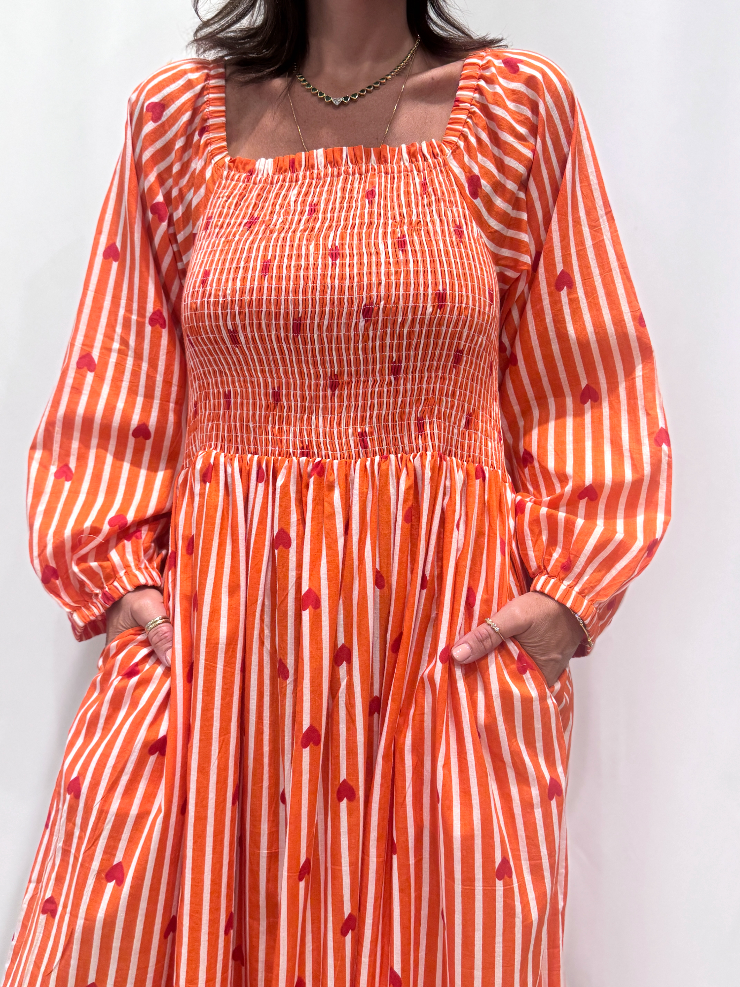 La robe Pyaar Orange, une robe longue manches longues, smockée à rayures et imprimés de coeurs. Une robe tendance pour cet été.