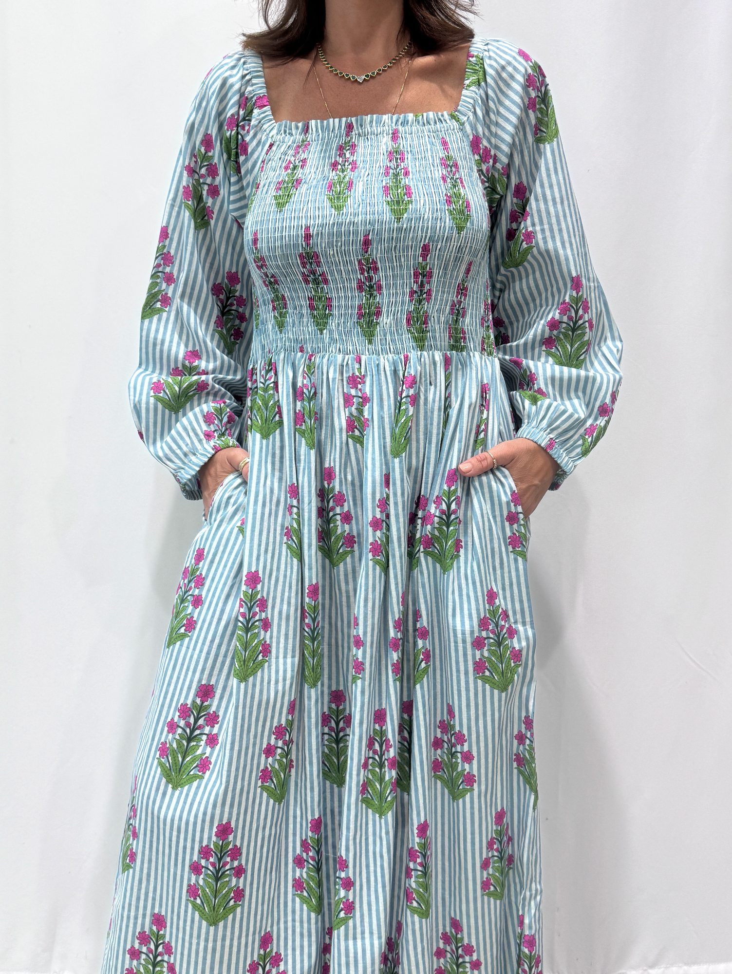 Robe Naya Bleu, une robe longue smockée. Fluide et 100 % coton. Elle est rayée avec des imprimés de fleurs.
