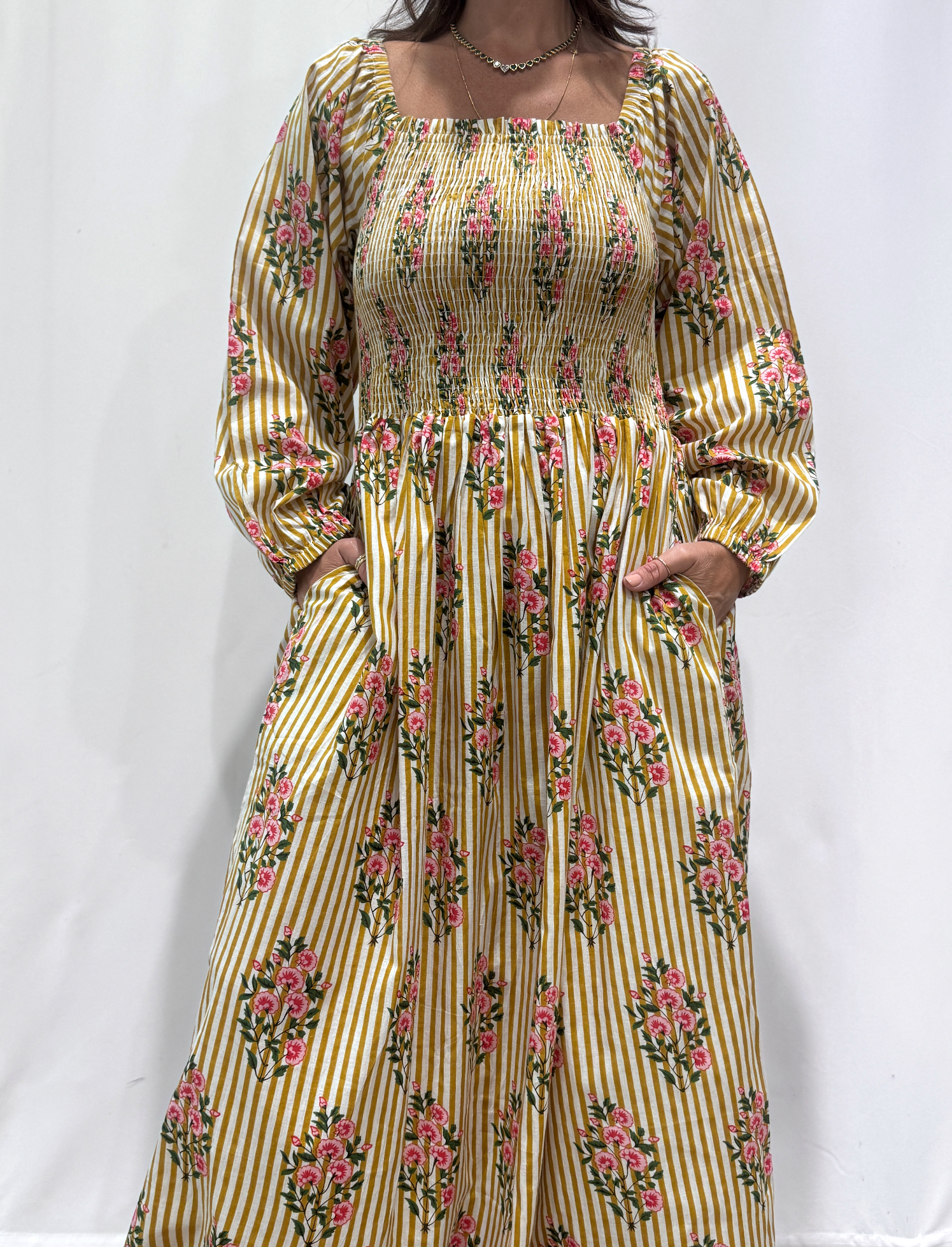 Robe Naya Jaune rayée, une robe longue smockée. Fluide et 100 % coton. Elle est rayée avec des imprimés de fleurs.