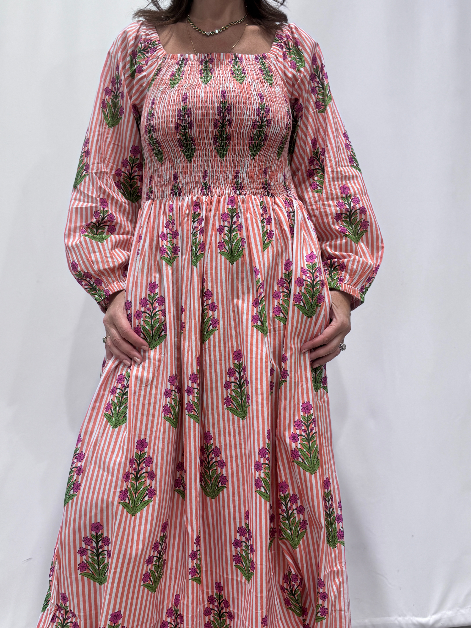 Robe Naya Saumon fleurs mauves, une robe longue smockée. Fluide et 100 % coton. Elle est rayée avec des imprimés de fleurs.
