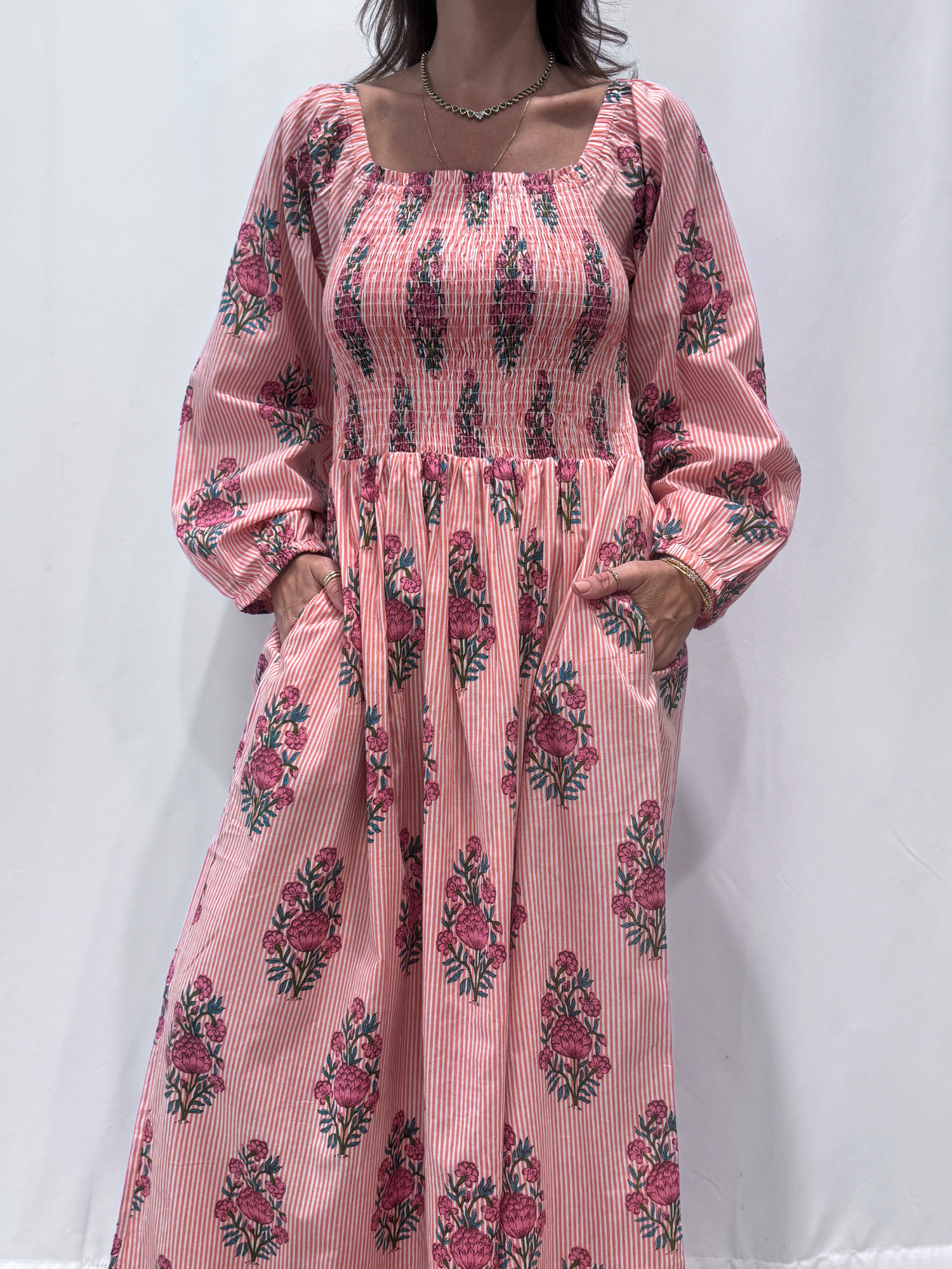 Robe Naya Saumon fleurs roses, une robe longue smockée. Fluide et 100 % coton. Elle est rayée avec des imprimés de fleurs.