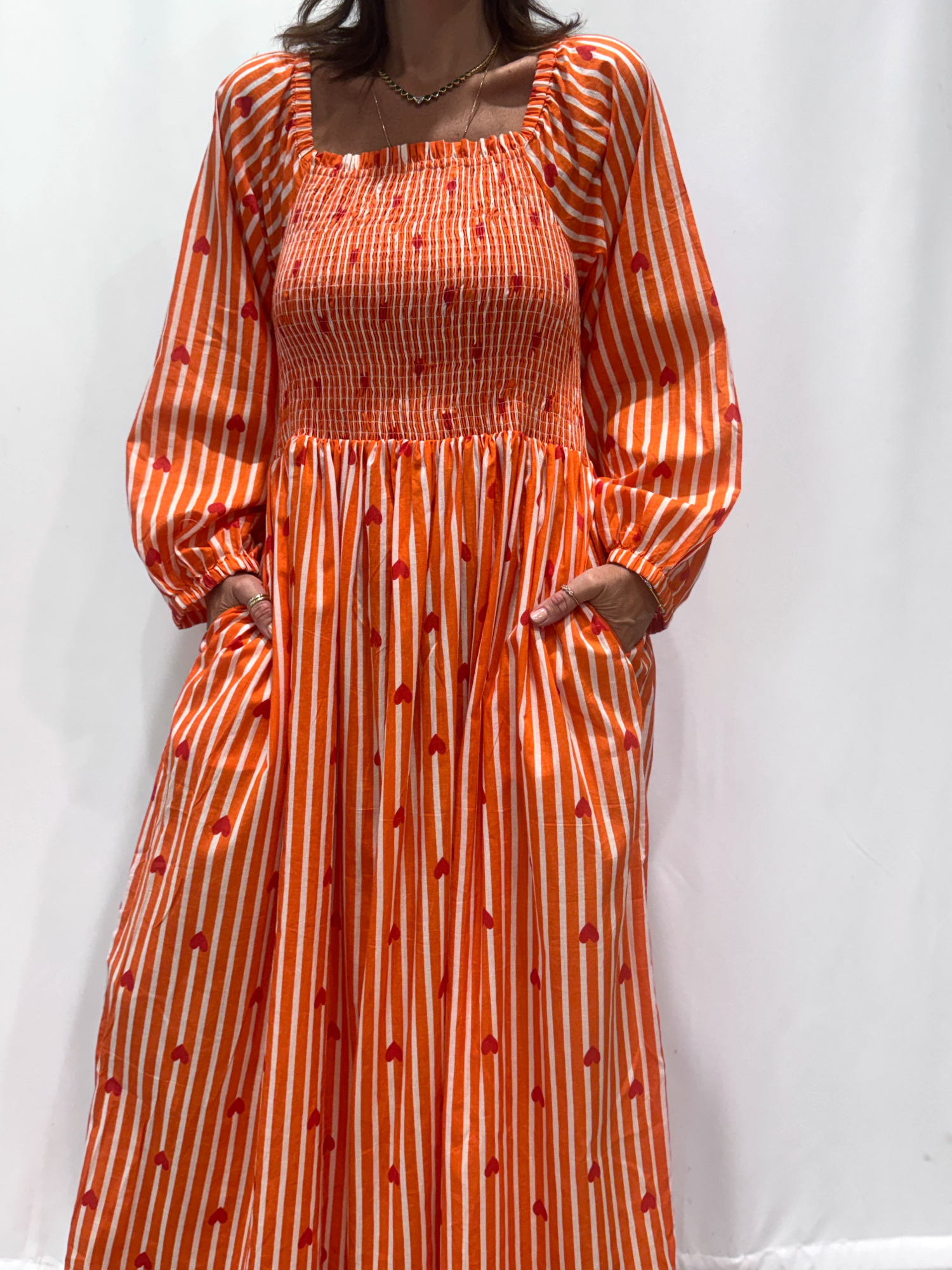 La robe Pyaar Orange, une robe longue manches longues, smockée à rayures et imprimés de coeurs. Une robe tendance pour cet été.