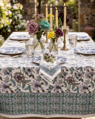La nappe Hampi, une nappe colorée et flrale pour la saison. Une nappe blanche avec des imprimés de fleurs mauves et verts.