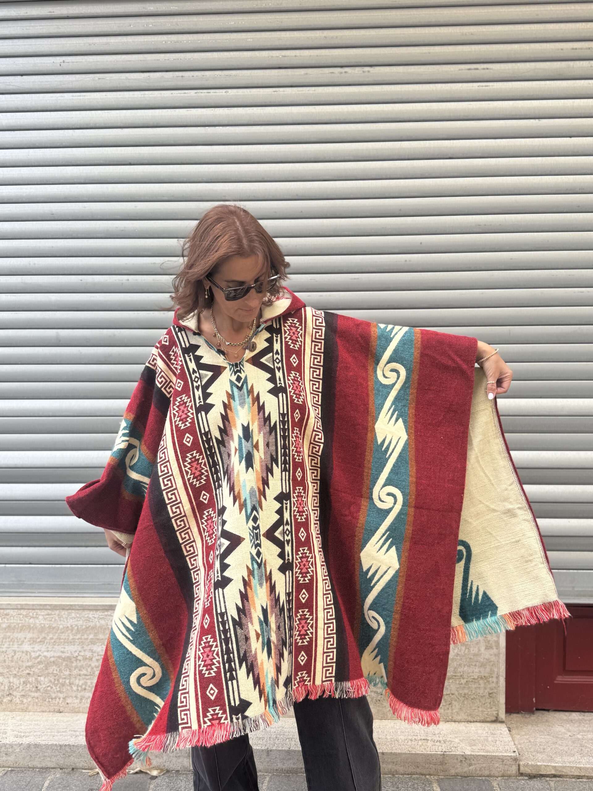 Stéphanie porte le poncho rouge avec des nuances de bleus, de crème et de noirs. Un poncho à capuche long.